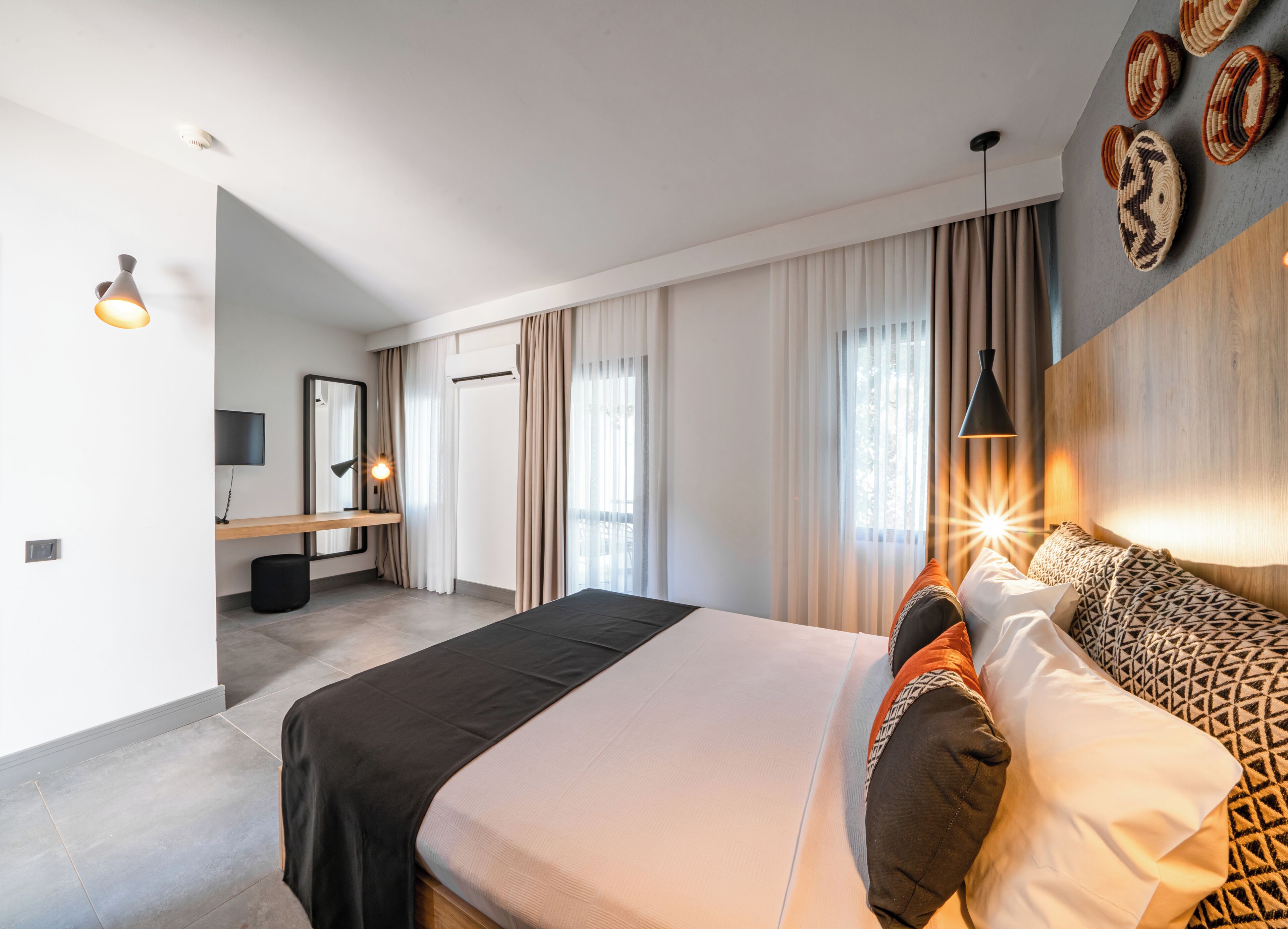 Une chambre d’hôtel moderne dotée d’un grand lit, d’un bureau avec une chaise, d’un téléviseur à écran plat et d’une grande fenêtre avec des rideaux.