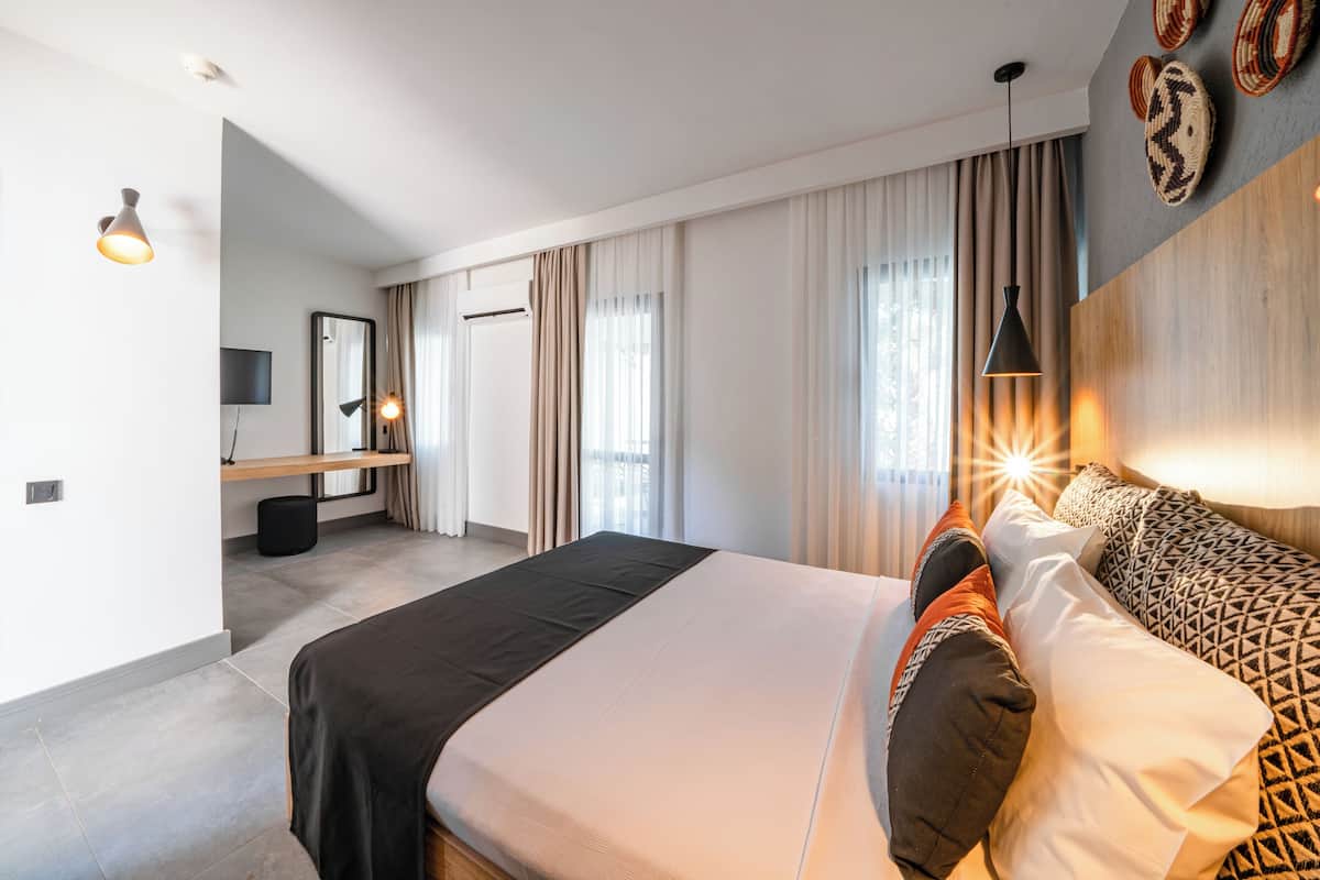 Une chambre d’hôtel moderne dotée d’un grand lit, d’un bureau avec une chaise, d’un téléviseur à écran plat et d’une grande fenêtre avec des rideaux.