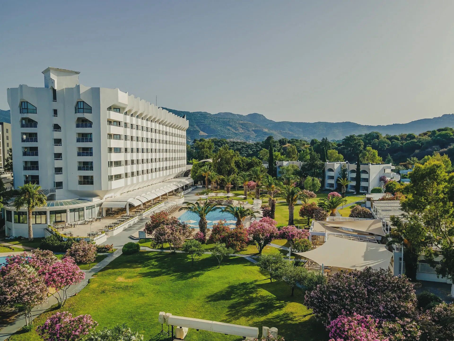 Un hotel con varios pisos, piscina y zonas verdes circundantes.