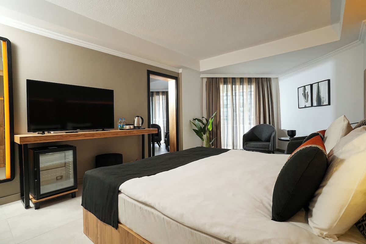 Une chambre d’hôtel avec un grand lit, un téléviseur à écran plat, un petit réfrigérateur, un bureau avec une chaise et une fenêtre avec des rideaux.
