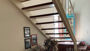 Eine Treppe mit hölzernen Geländern führt zu einer Zwischenebene mit einer Holzbank und einem Tisch mit Blumen.'