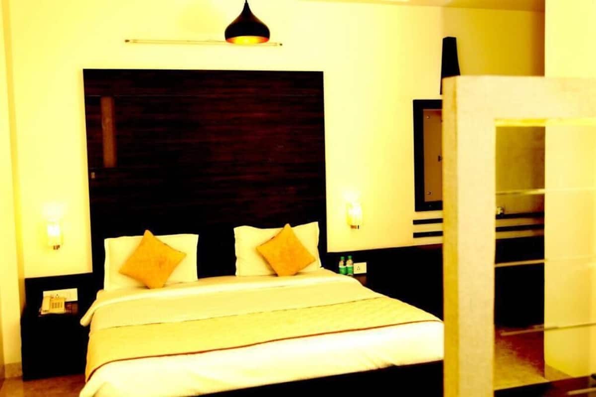 A hotel room with a large bed, two bedside tables, a nightstand, a wall-mounted TV, and a door leading to another room.