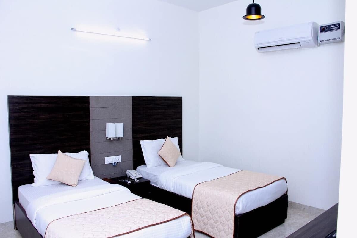 A hotel room with two beds, a dark wood headboard, bedside lamps, an air conditioning unit, and a wall-mounted phone.