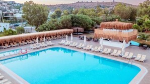 En swimmingpool med solstolar och parasoller, omgiven av byggnader och träd.