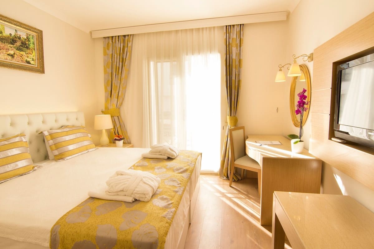 A hotel room with a bed, a desk, a chair, a mirror, and a television.