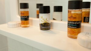 A bathroom shelf with various toiletries including body lotion and shampoo. - Kontogoni Rooms (Elafonisos)