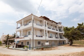 A multi-story building with balconies, a covered outdoor seating area, and a tree in the foreground. - Kontogoni Rooms (Elafonisos)