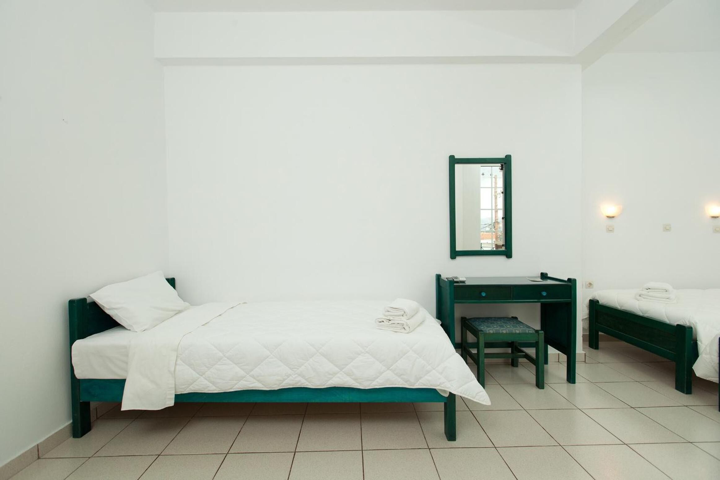 Een kamer met twee bedden, een bureau, een stoel, een spiegel en een klein tafeltje.