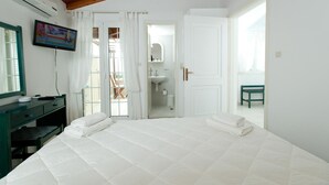 A bedroom with a large bed, a TV mounted on the wall, a desk, and a chair. - Kontogoni Rooms (Elafonisos)