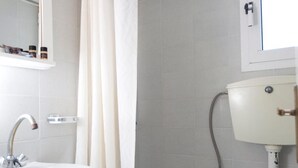 A bathroom with a white sink, mirror, toilet, and shower curtain. - Kontogoni Rooms (Elafonisos)