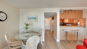 A dining area with wicker chairs and a glass table, a kitchen with a wooden countertop, and a red chair.