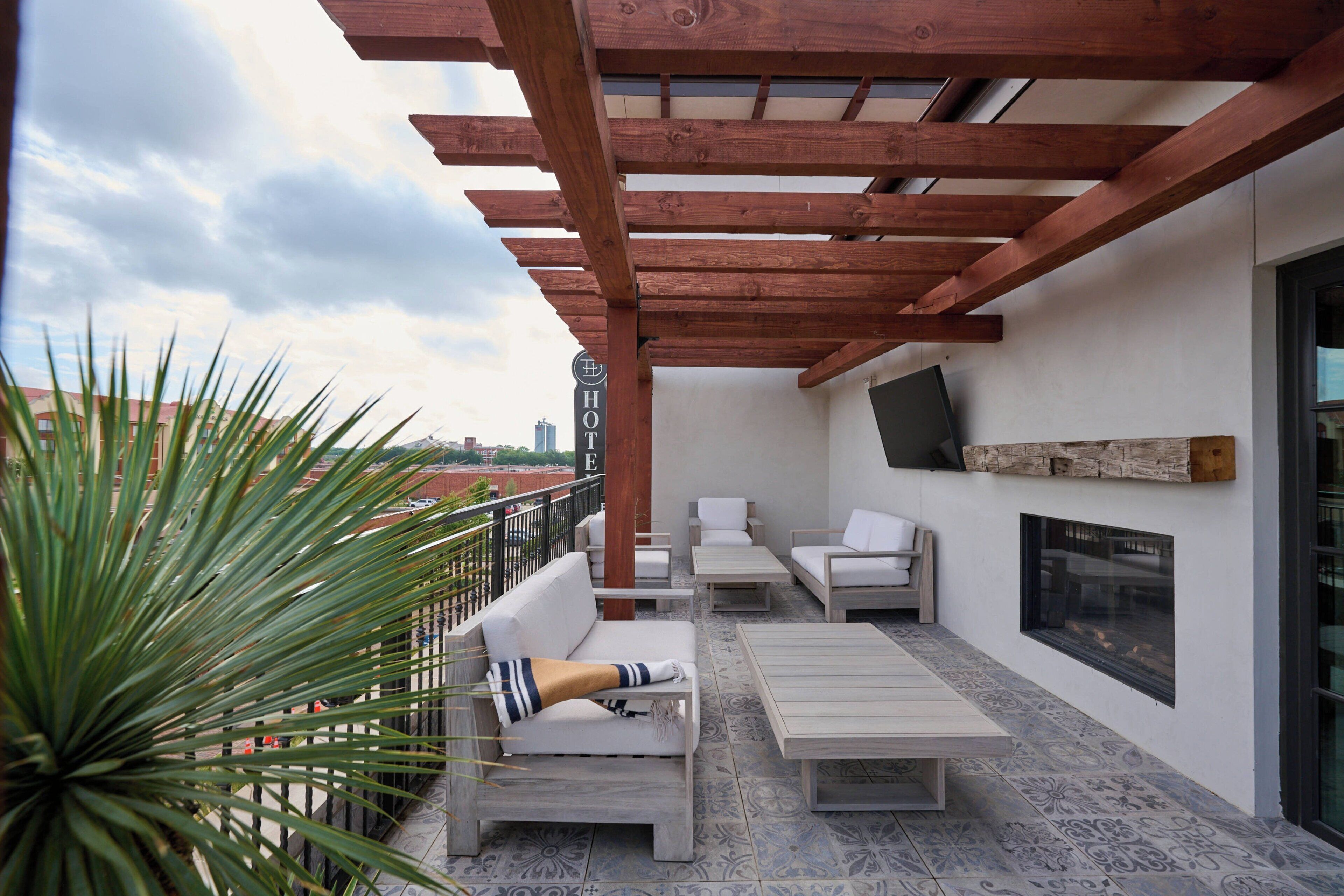 A rooftop patio with outdoor seating, a TV mounted on the wall, and a view of the cityscape.