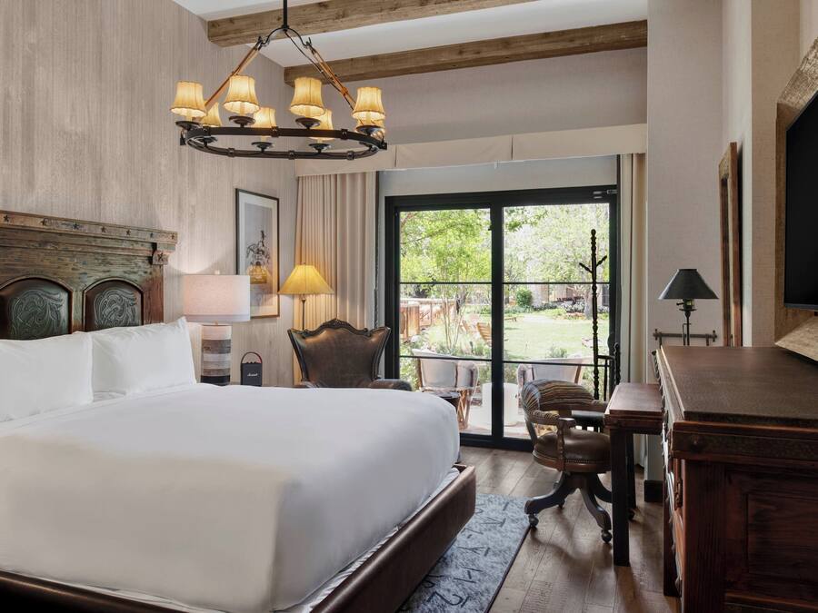 A hotel room with a large bed, a wooden headboard, a chandelier, a desk, and a view of the outdoors.