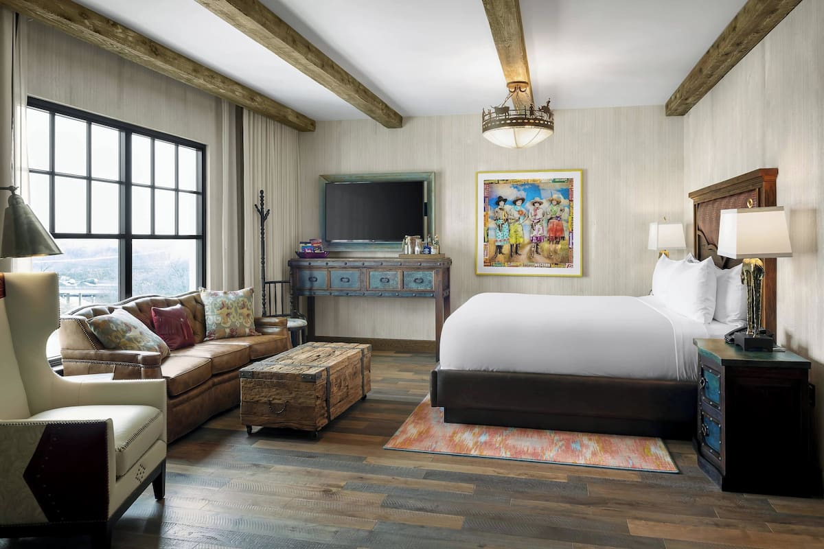 A spacious bedroom with a large bed, a wooden chest, a sofa, and a desk with a mirror.