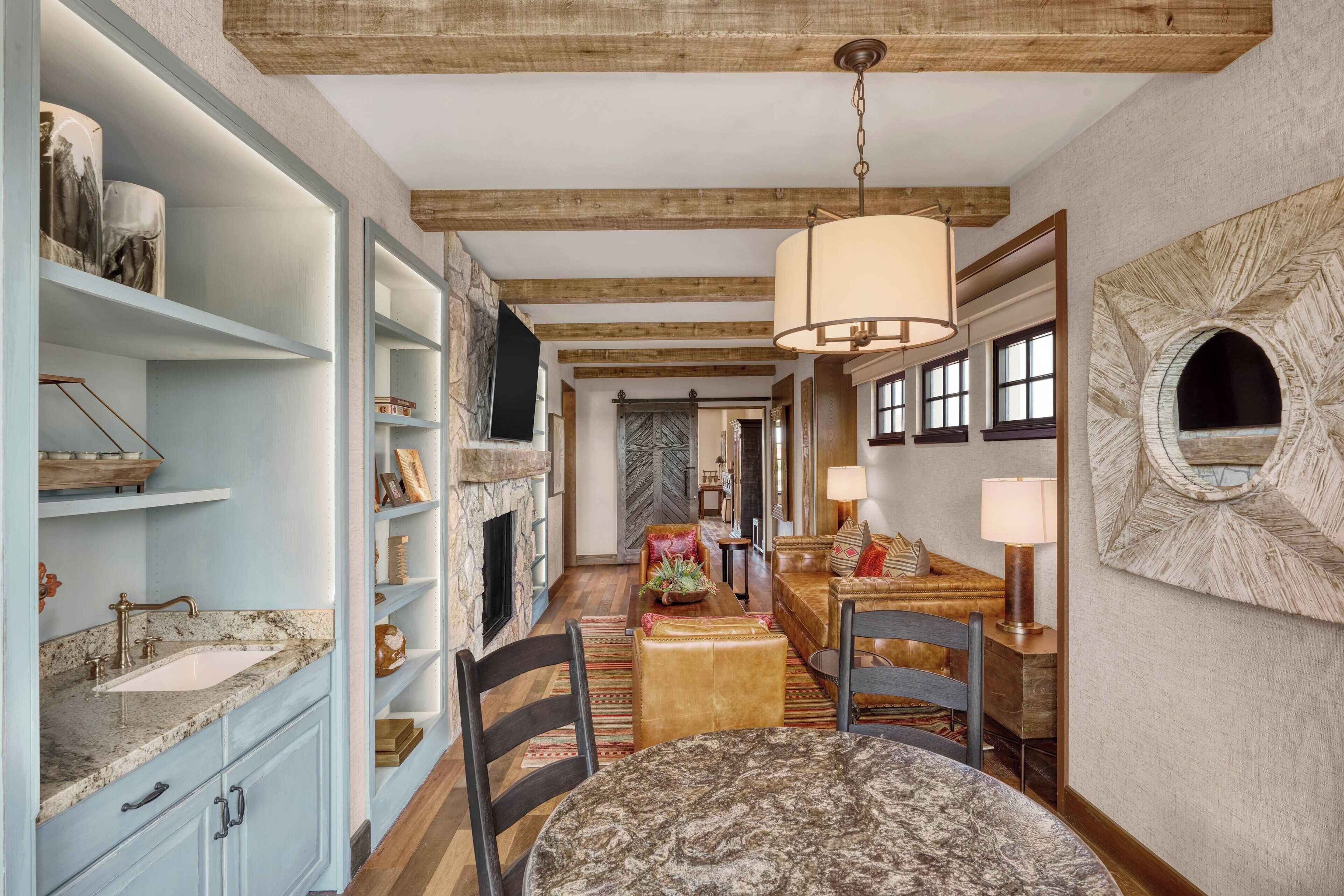 A spacious room with a marble sink, wooden shelves, a dining area with a round table, and a fireplace.
