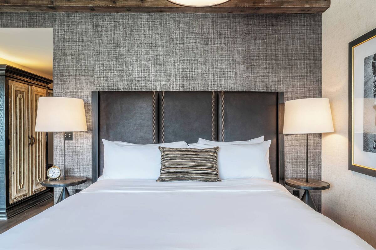 A neatly made bed with a dark headboard, two bedside lamps, and a clock on a bedside table.