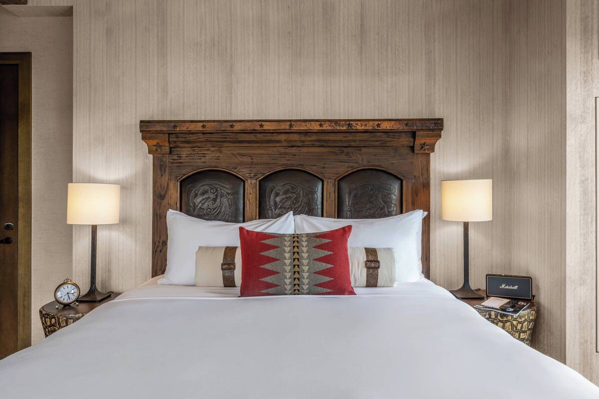 A neatly made bed with a wooden headboard, two bedside lamps, and a red decorative pillow.