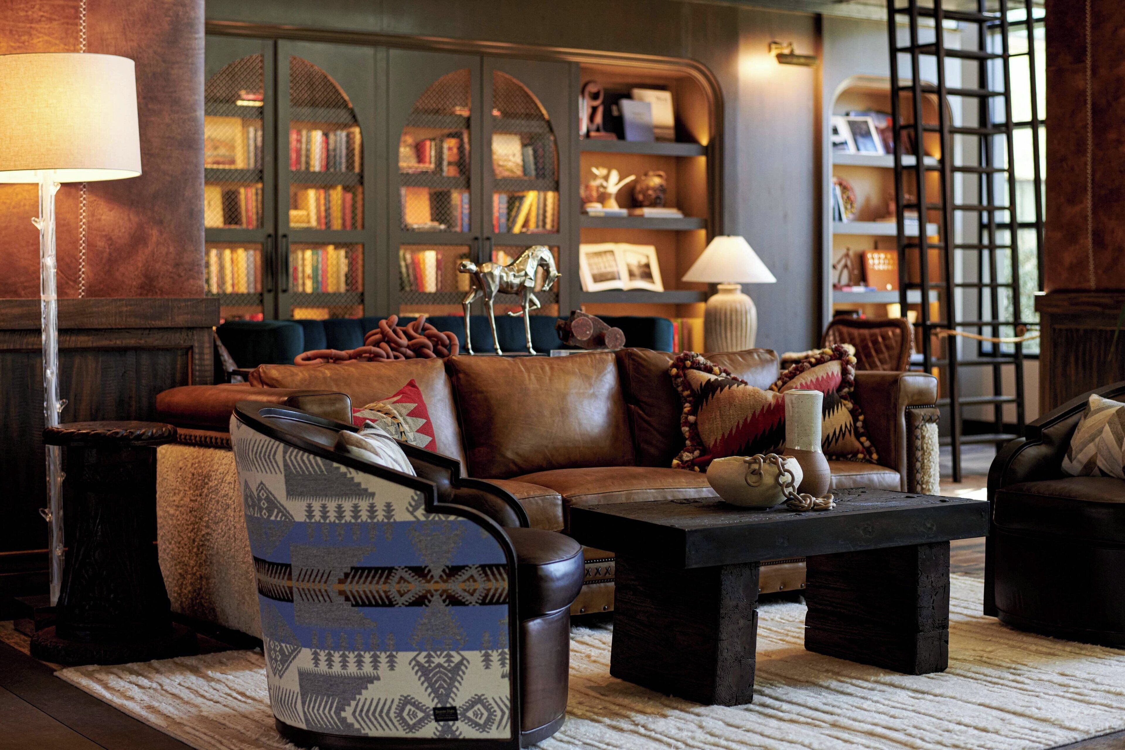 Ein gemütliches Wohnzimmer mit Ledersofa, gemustertem Sessel und Couchtisch. Bücherregale sind mit Büchern und Dekoration gefüllt.