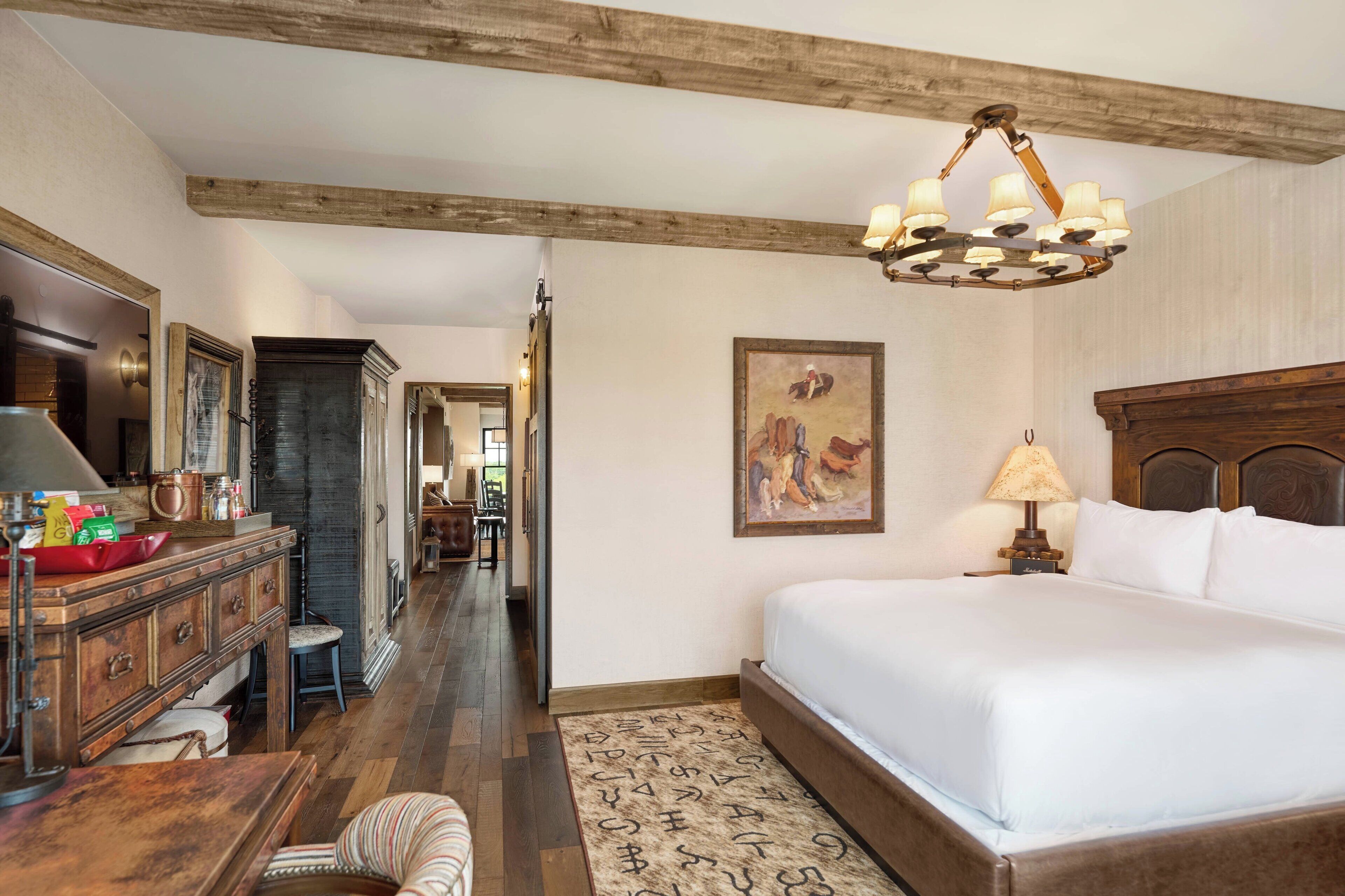 A hotel room with a large bed, wooden headboard, a desk with a lamp, a chair, and a rug.