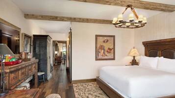 A hotel room with a large bed, wooden headboard, a desk with a lamp, a chair, and a rug.