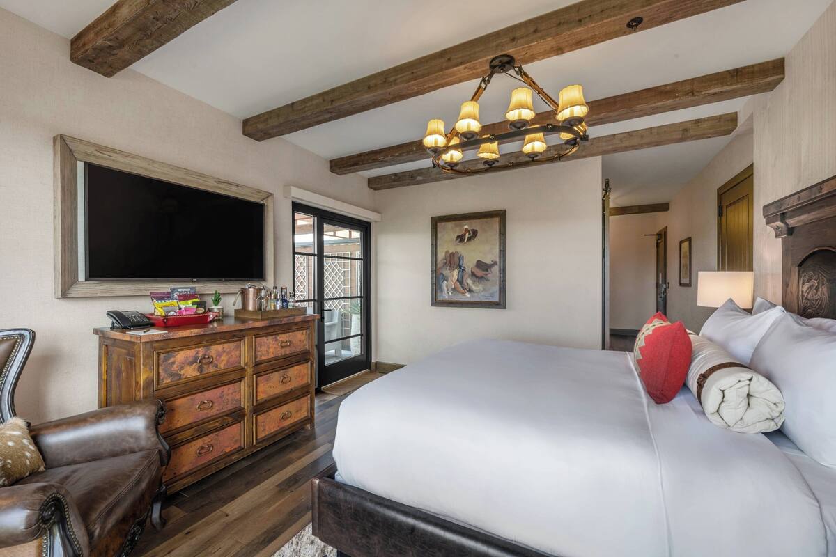 A bedroom with a large bed, wooden dresser, and a flat-screen TV mounted on the wall.