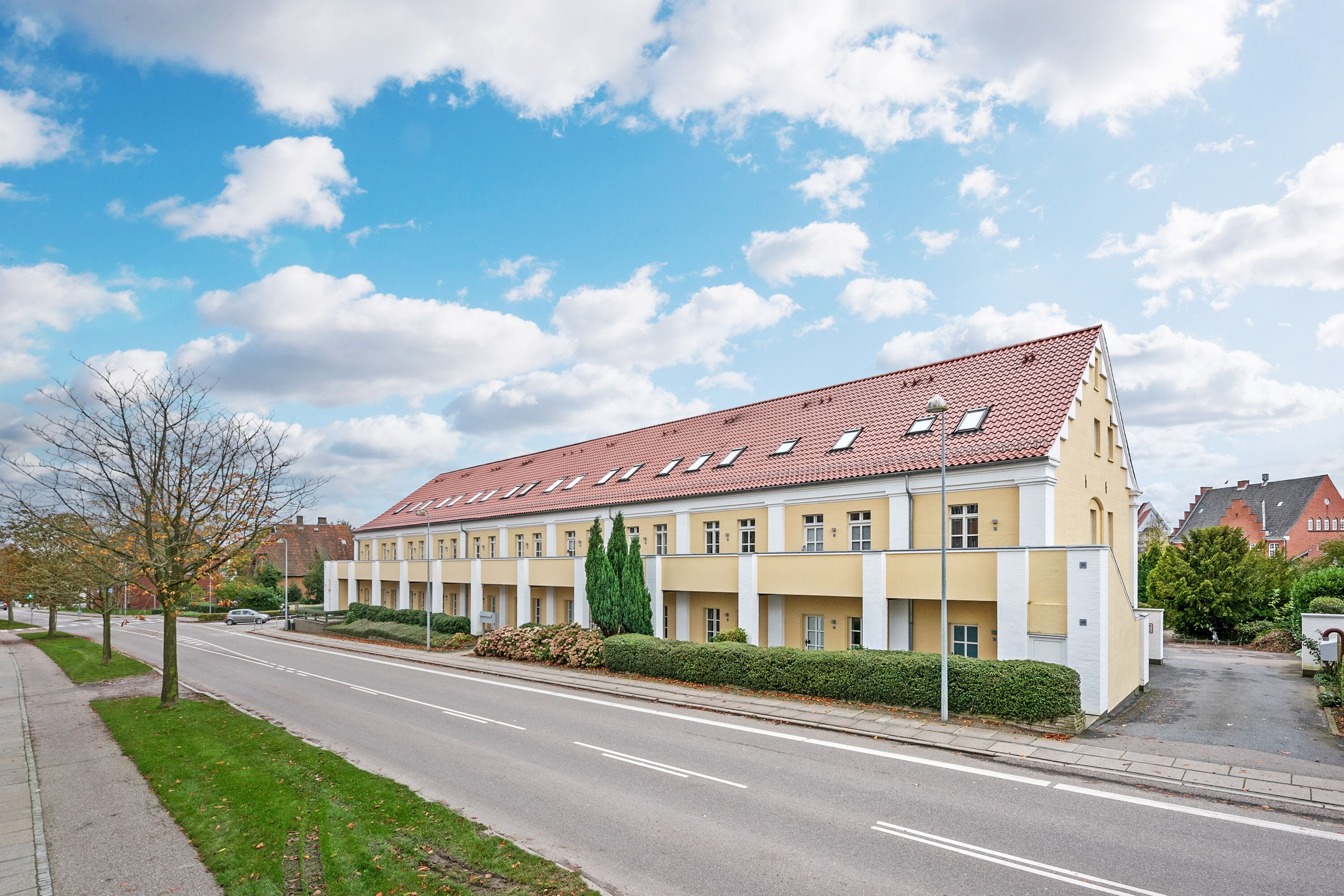 A long, yellow building with a red-tiled roof and multiple windows along a street.