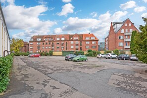 A parking lot with several cars, surrounded by multi-story buildings with red brick facades and a clear sky.
