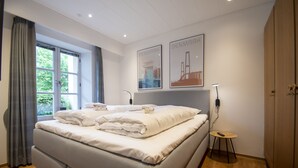 A modern bedroom with a large bed, two wall-mounted lights, a small side table, and two framed pictures of Denmark. - City Center Luxury Getaway (Sønderborg)