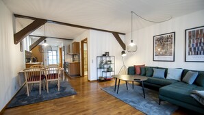 A spacious living area with a wooden floor, a green sofa, a dining table with chairs, and a kitchen in the background. - City Center Luxury Getaway (Sønderborg)