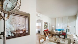 Una sala de estar moderna con una mesa de comedor de vidrio, sillas de madera, un espejo grande y un modelo de barco.