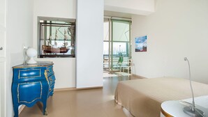 Un dormitorio moderno con cama, cómoda, escritorio y un amplio ventanal con vista al puerto deportivo.