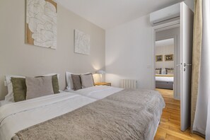 A bedroom with two beds, a nightstand, a lamp, and a door leading to another room.