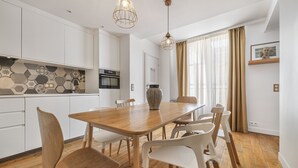 Une cuisine moderne avec une table et des chaises en bois, un luminaire suspendu et une grande fenêtre avec des rideaux.