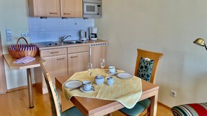 Eine kleine Küche mit Holzausstattung, einer Mikrowelle und einem Spülbecken. Es gibt einen Esstisch mit Stühlen, einen Korb und eine Kaffeemaschine.