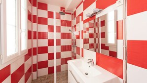 Une salle de bain avec des carreaux rouges et blancs formant un motif à carreaux, un lavabo blanc et un espace douche.