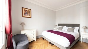 Une chambre à coucher avec un lit, une chaise, une commode et un tableau accroché au mur.