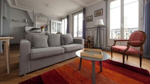 Un salon avec un canapé gris, une table basse ronde, un fauteuil à rayures et un tapis rouge.
