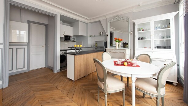 Une cuisine moderne dotée d’un îlot central, de meubles blancs et d’un coin repas avec une table ronde et des chaises.