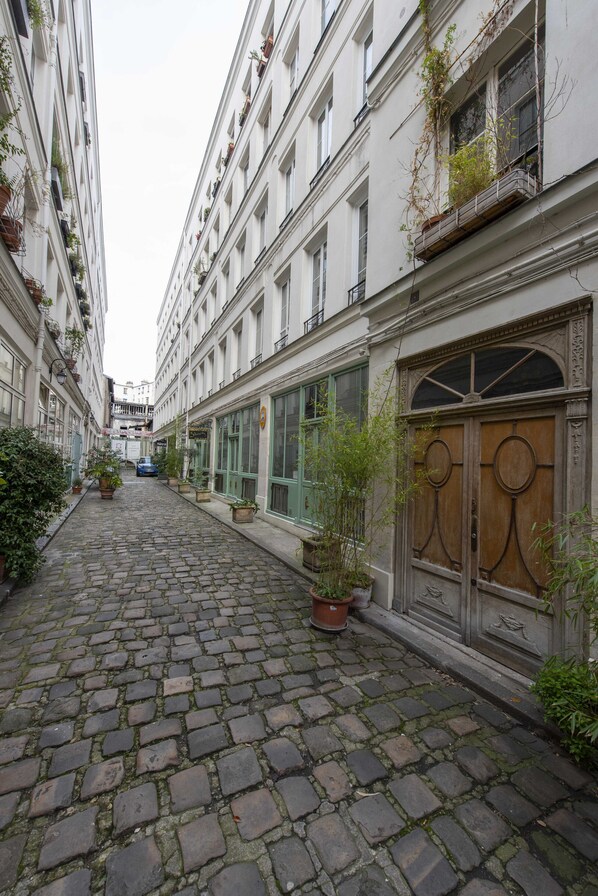 A cobblestone street flanked by buildings with balconies, potted plants, and a wooden door.