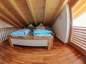Een slaapkamer in een loft met een houten plafond, een bed met bloemenbeddengoed en een uitzicht door een raam.
