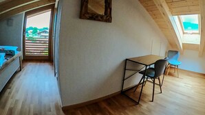 Een loft-achtige kamer met een schuine plafond, een klein tafeltje met stoelen, een bed en een groot raam.