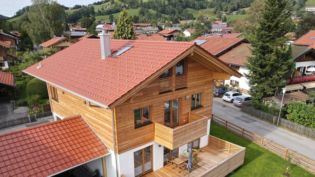 Een modern herenhuis met een rode pannendak, een houten terras en een garage.