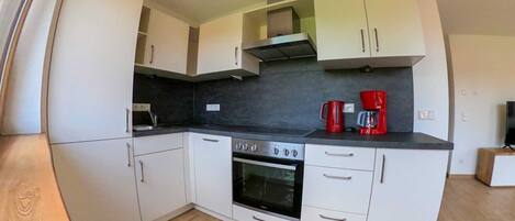 A compact kitchen with white cabinets, a black countertop, a stove, and a red coffee maker.