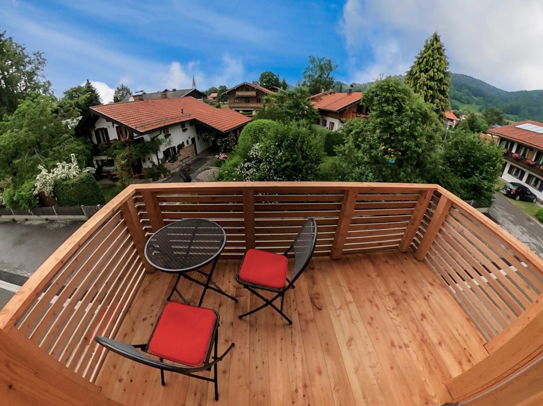 Una terraza de madera con una mesa y sillas, con vistas a un pueblo con casas y vegetación.