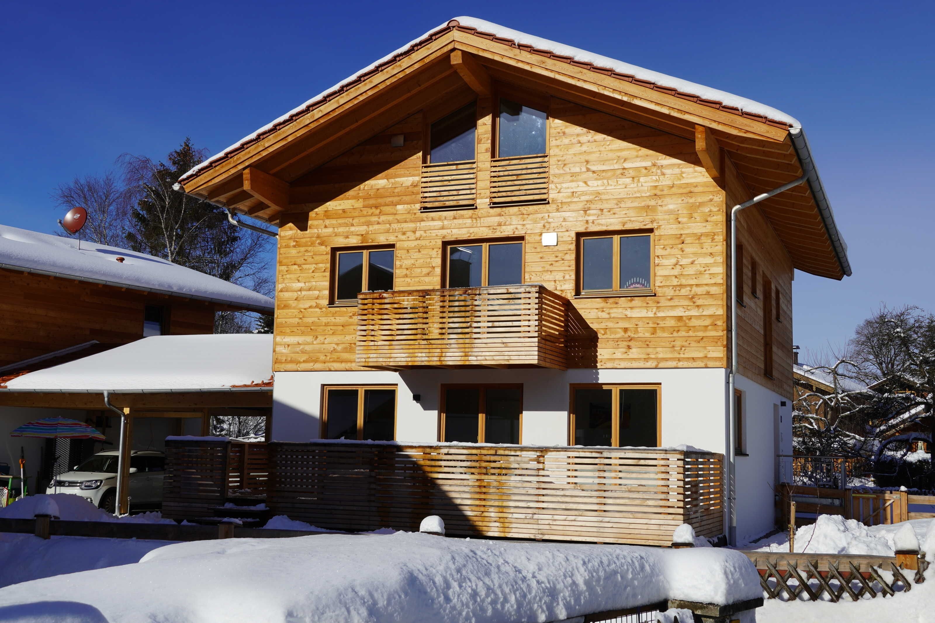 A wooden chalet with a balcony, a garage, and a snow-covered roof.