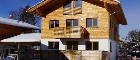 A wooden chalet with a balcony, a garage, and a snow-covered roof.