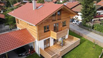 Ein modernes, zweistöckiges Haus mit rotem Ziegeldach, einer Holzterrasse und einer Garage.
