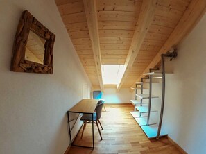 Een kleine kamer met een houten plafond, een tafel met stoelen, een spiegel en een trap.