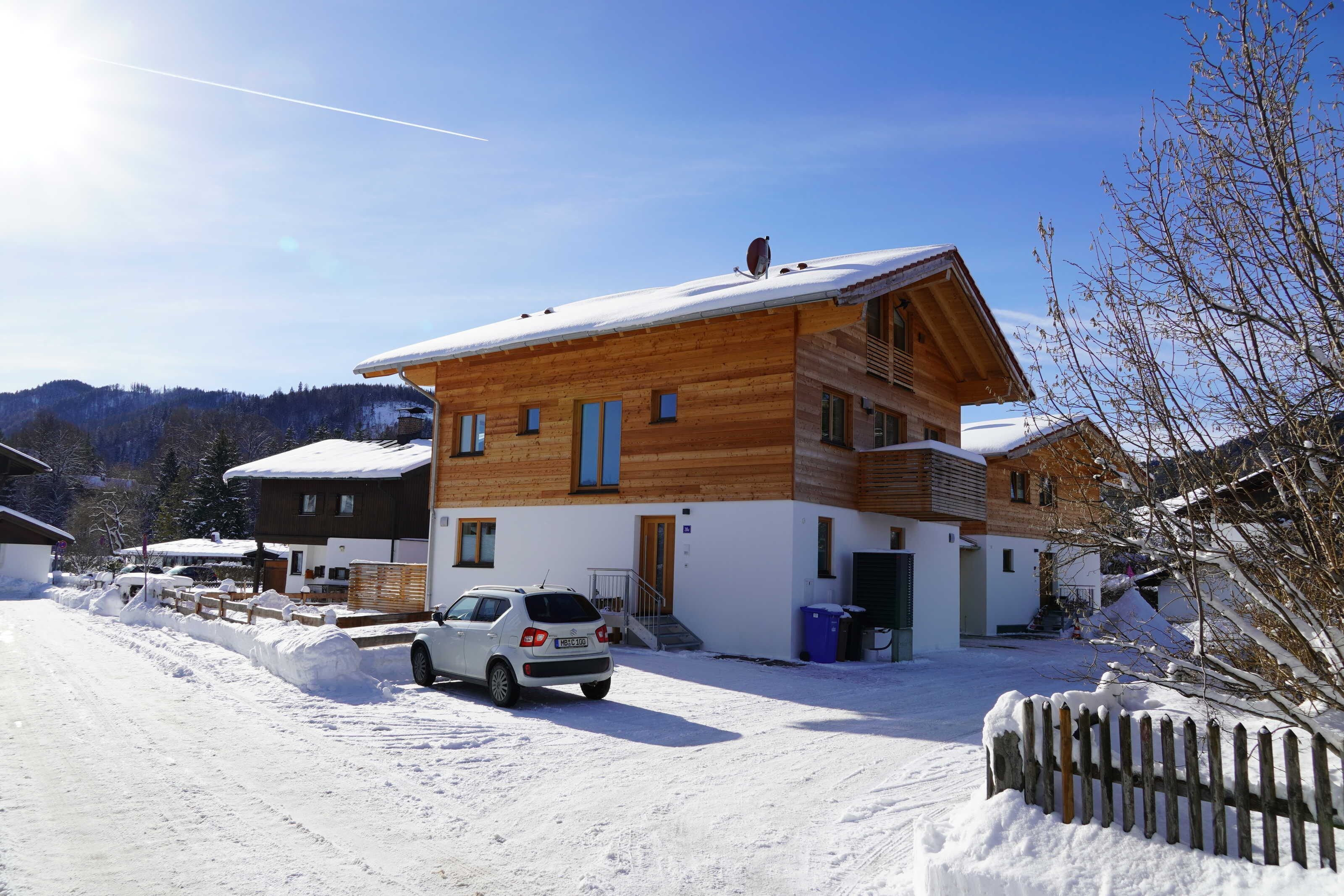 Ein zweistöckiges Holzhaus mit einem Auto davor, umgeben von Schnee.