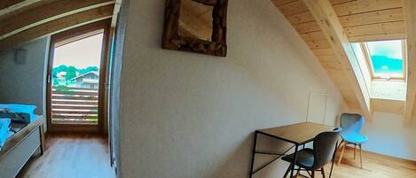Un espacio tipo loft con techo inclinado, una pequeña mesa con sillas, una cama y un ventanal grande.